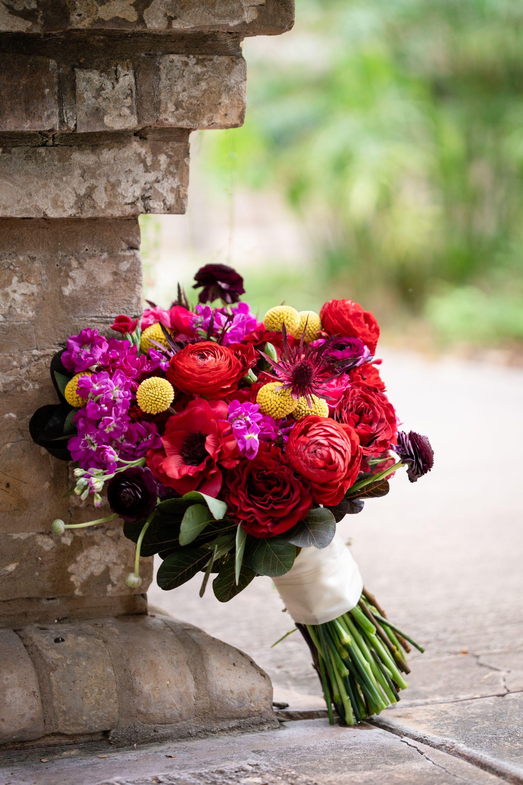 Vibrant wedding bouquets with red, pink and purple flowers arranged on stone ledge.