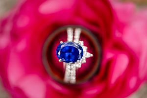 A sapphire blue engagement ring nestled in the petals of a vibrant pink rose flower.