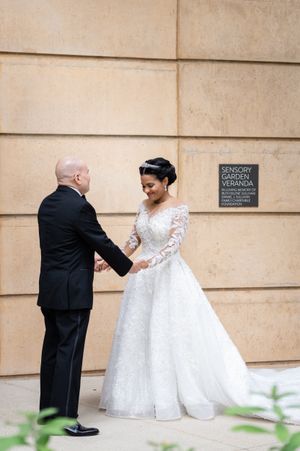 Wedding couple walking along a stone building exterior during a first look moment.