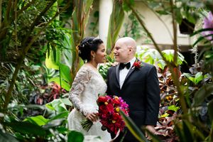 Wedding couple posing together in a lush greenhouse setting with tropical plants.