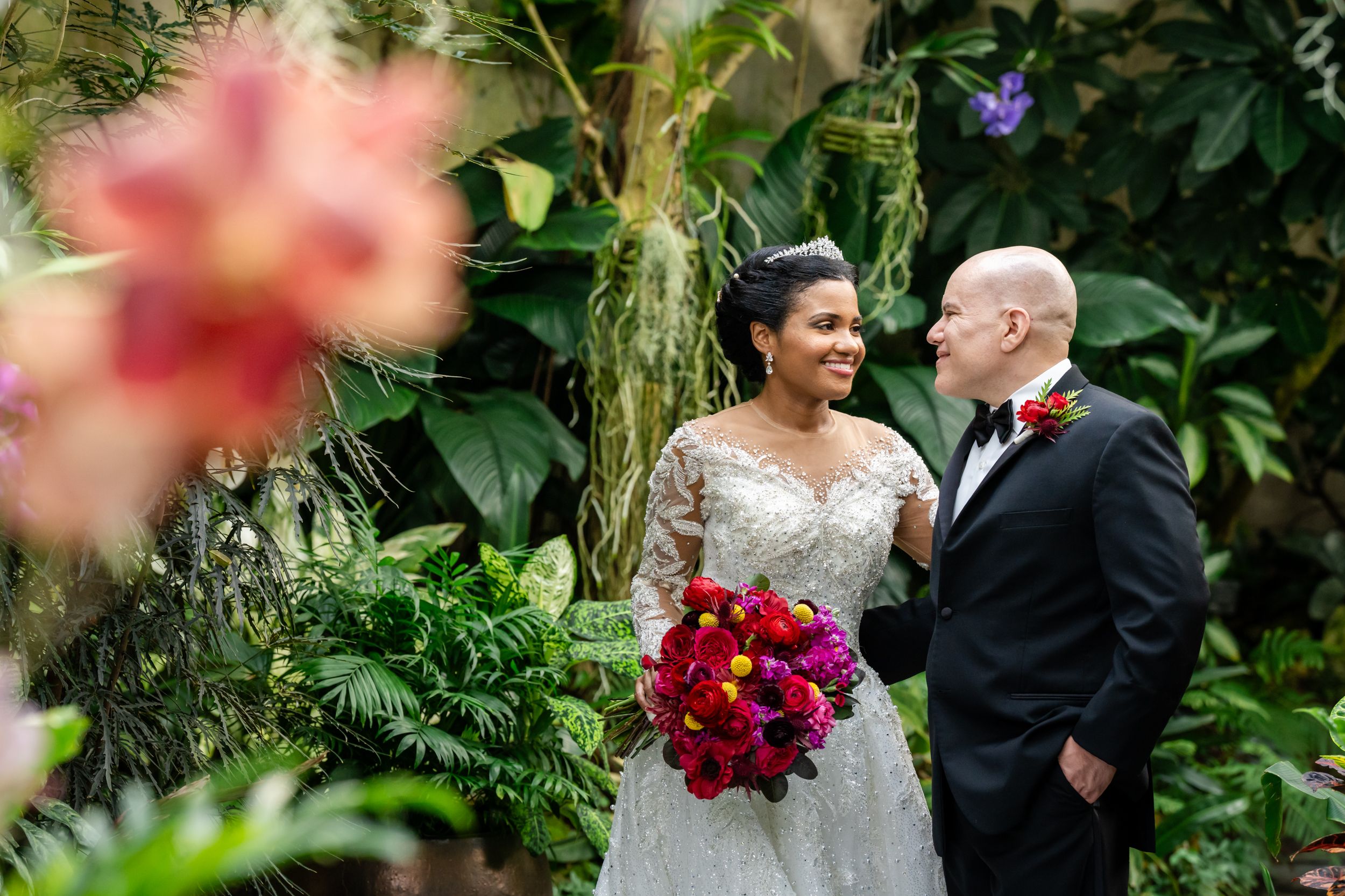 A couple shares a romantic moment in a lush garden setting with vibrant pink and red flowers.
