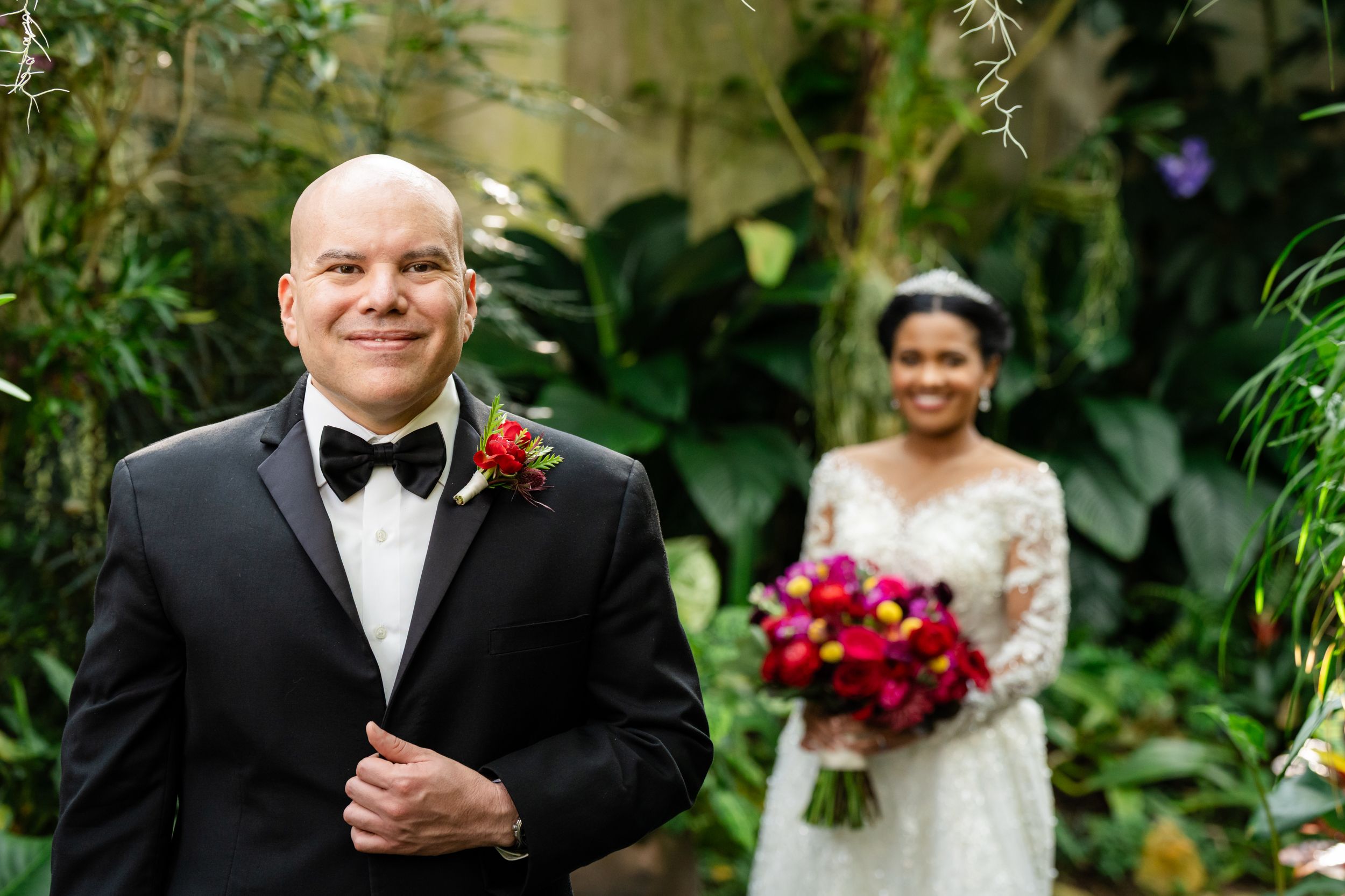 Wedding party gathered in a tropical garden setting with red bouquets and formal attire.