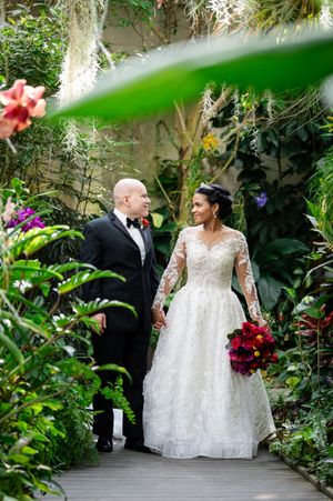 Wedding couple strolling through lush greenhouse garden with tropical plants.