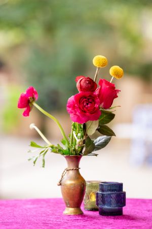 Small red flowers in rustic vases and decorative bowls arranged on a pink surface with soft blurred background.