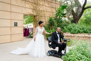 Wedding party taking outdoor photos in a garden setting with natural stone walls.