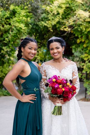 Bridesmaids in teal dresses pose with bride holding vibrant pink and red bouquet.