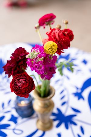 Vibrant red and pink floral centerpieces in gold vases on blue and white patterned tablecloth.