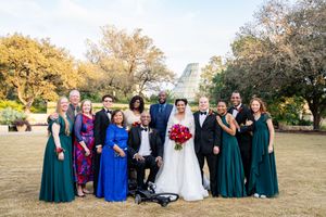 Wedding party members in blue and green dresses pose together outdoors during autumn.