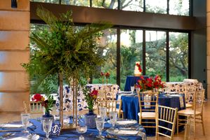 Elegant wedding reception setup with blue and gold decor in a bright venue with large windows overlooking trees.