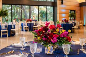 Elegant wedding reception venue with wooden ceiling beams, blue tablecloths, and vibrant red floral centerpieces.