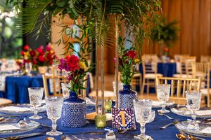 Elegant wedding reception table settings with blue and white decor, crystal glasses, and tropical palm leaf accents.