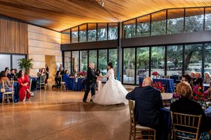 Wedding reception in a modern venue with wood paneled ceiling and floor-to-ceiling windows as guests watch a dance.