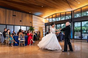 A panoramic view of a modern reception venue with wood paneled ceiling and large windows showing guests at tables.