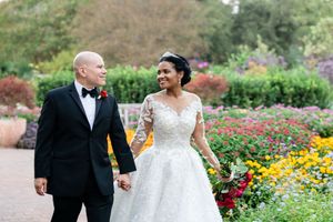 A couple walks hand in hand through a vibrant garden filled with colorful yellow and red flowers.