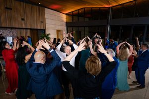 Wedding guests on a dance floor raise their arms in celebration during a reception party.