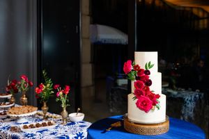 Elegant wedding dessert table with red roses, cake, and treats on blue and white linens.