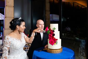 A wedding cake decorated with red flowers sits on a table at an elegant reception venue.
