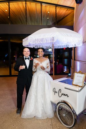 Vintage white ice cream cart with parasol serves treats at an elegant indoor wedding reception.