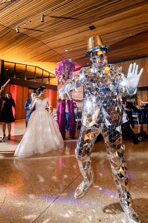 Wedding guests dance with illuminated LED robot performers on a shiny ballroom floor.
