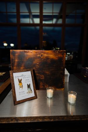 Rustic wooden table displays small framed cards and glowing white candles in a dimly lit evening setting.