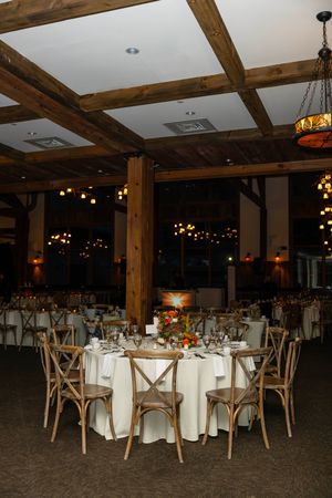 Rustic wedding reception venue with wooden beams, crossback chairs, and round tables set with white linens and warm lighting.