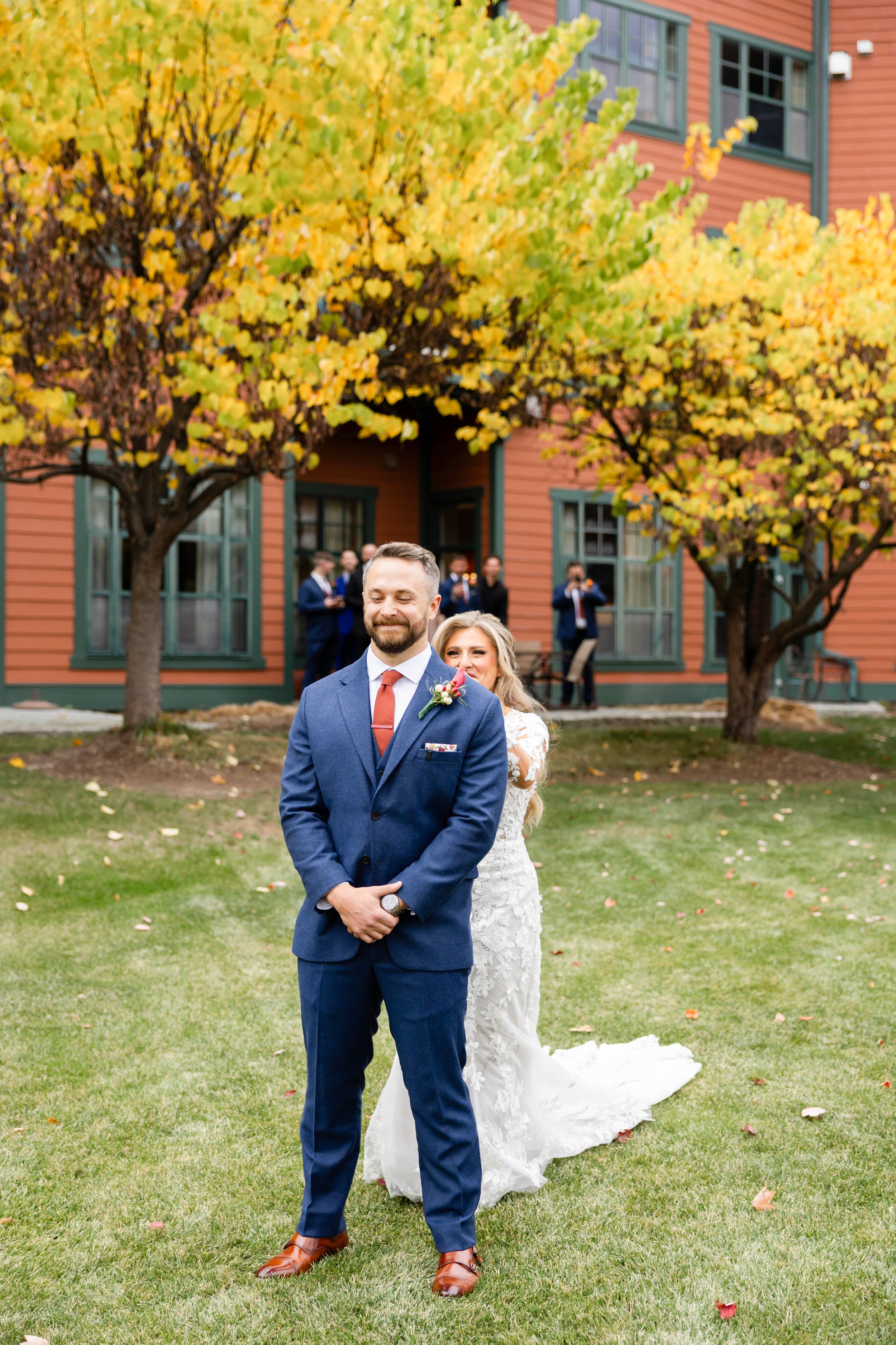 A couple poses for wedding photos under vibrant yellow autumn trees next to a brick building. | NJ wedding photographer