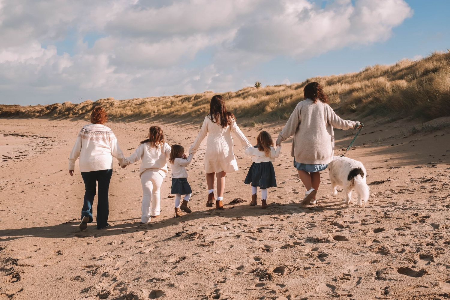 A group of people in white clothing walk along a sandy beach during golden hour.