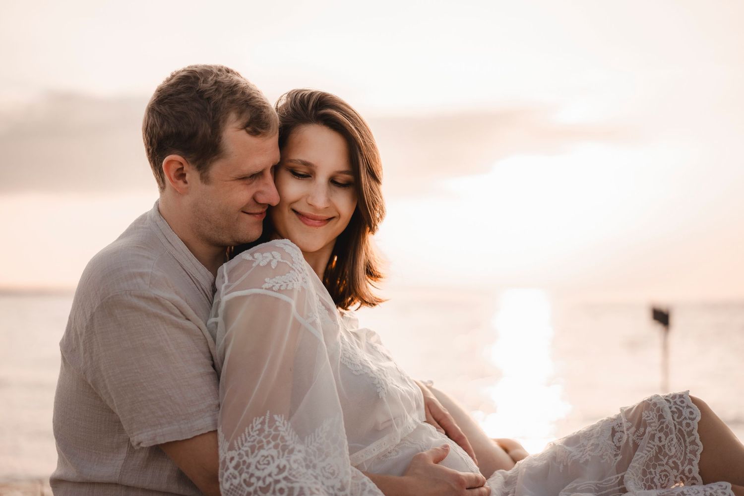 Candid and joyful portrait of a pregnant woman smiling by the sea, professional destination photography.