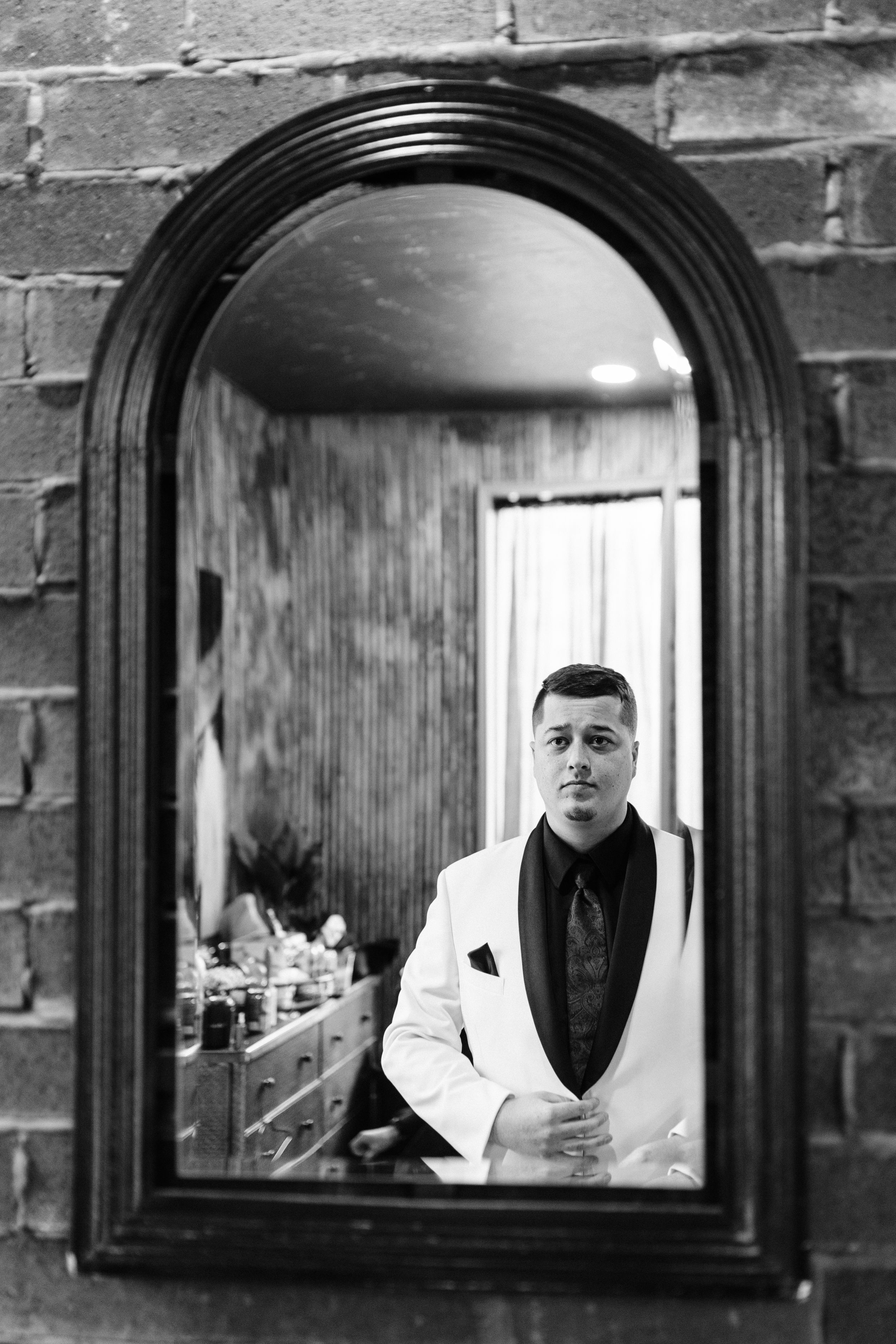 A sequence of black and white mirror reflections showing a person in a white jacket against a dark brick wall background.