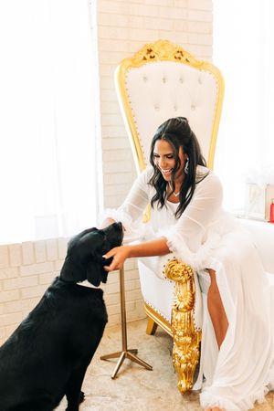A playful photo series of a person in white interacting with a black dog on an ornate gold and white chair.