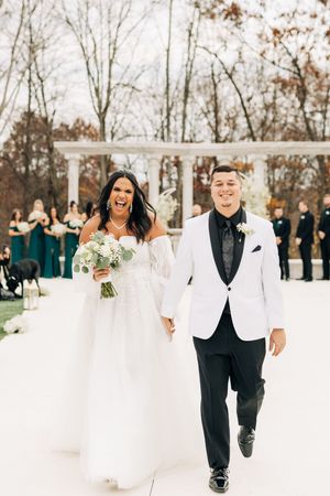 Wedding party members walk through snow in white dresses and black suits during winter celebration.