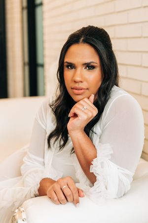 Portrait of a woman in a white ruffled blouse posing thoughtfully on a cream-colored couch.