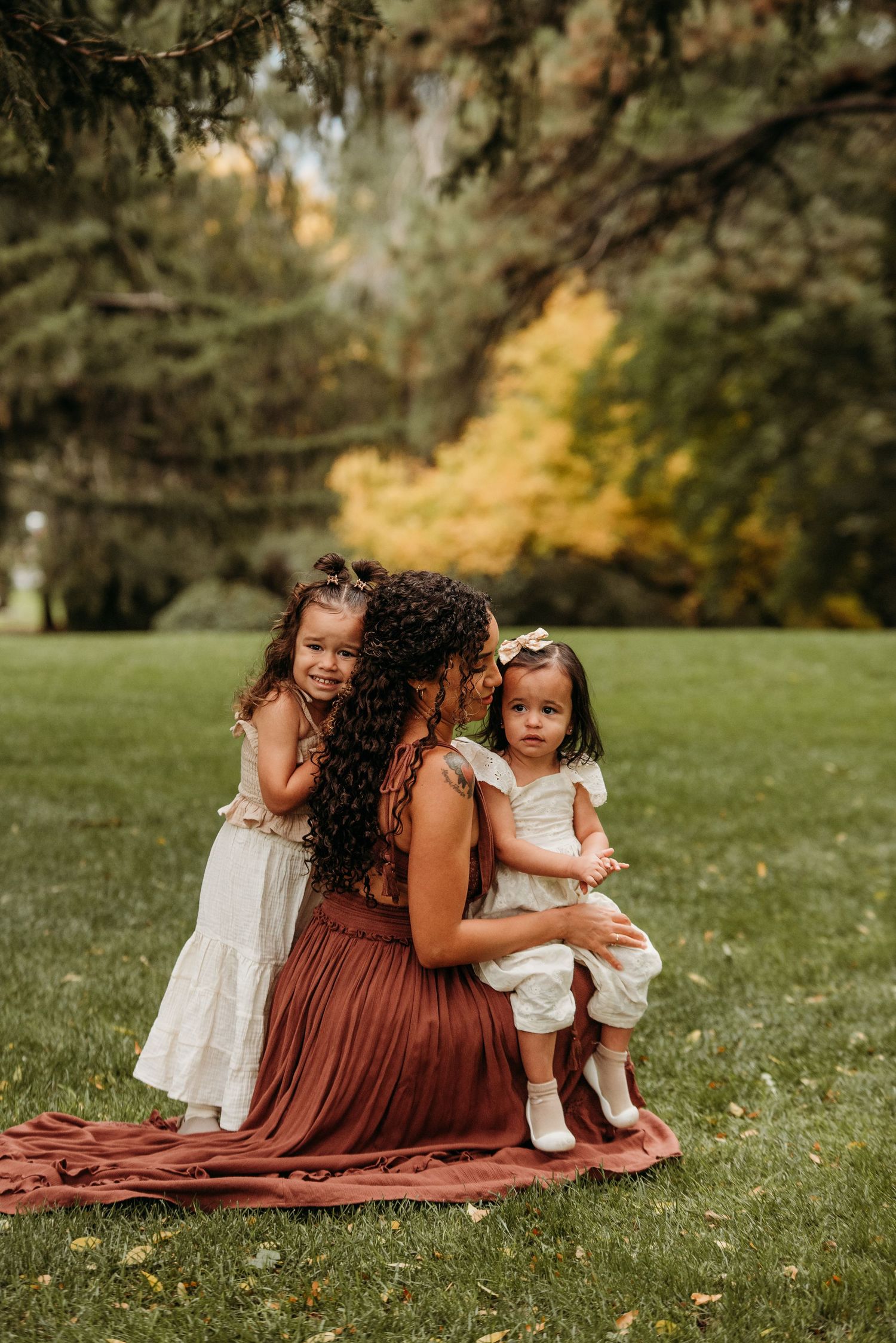 A tender family moment captured outdoors on a blanket in a park with Spanish moss draped trees in the background.