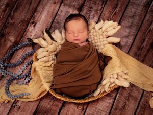 Newborn baby boy wrapped up in a brown swaddle in a basket during a newborn photography session in Calgary, Alberta