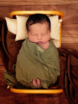 Newborn baby boy wrapped up in a green swaddle in a tiny bed during a newborn photography session in Calgary, Alberta.