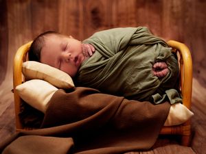 Newborn baby boy wrapped in a green swaddle on his side in a tiny bed during a newborn photography session in Calgary, Alberta
