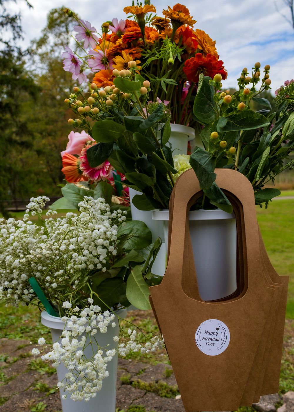 Colorful birthday flower bouquets with orange zinnias and white baby's breath in white buckets with a kraft paper gift bag.