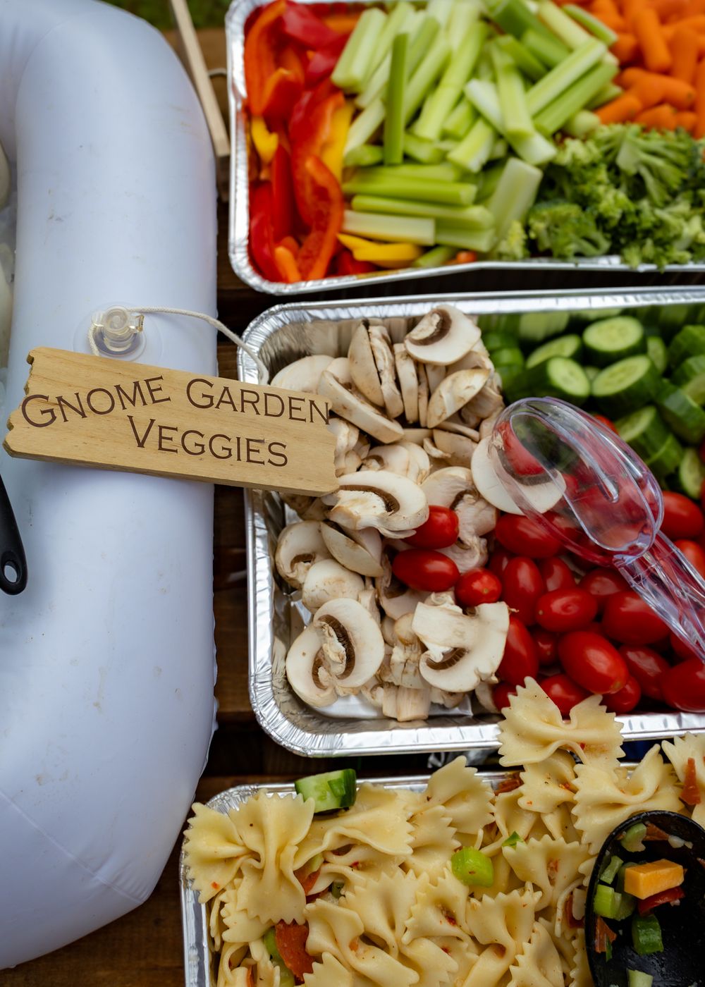 Gnome Garden Veggies sign with mushrooms, cherry tomatoes, celery, peppers, broccoli, cucumbers, and bowtie pasta in trays.