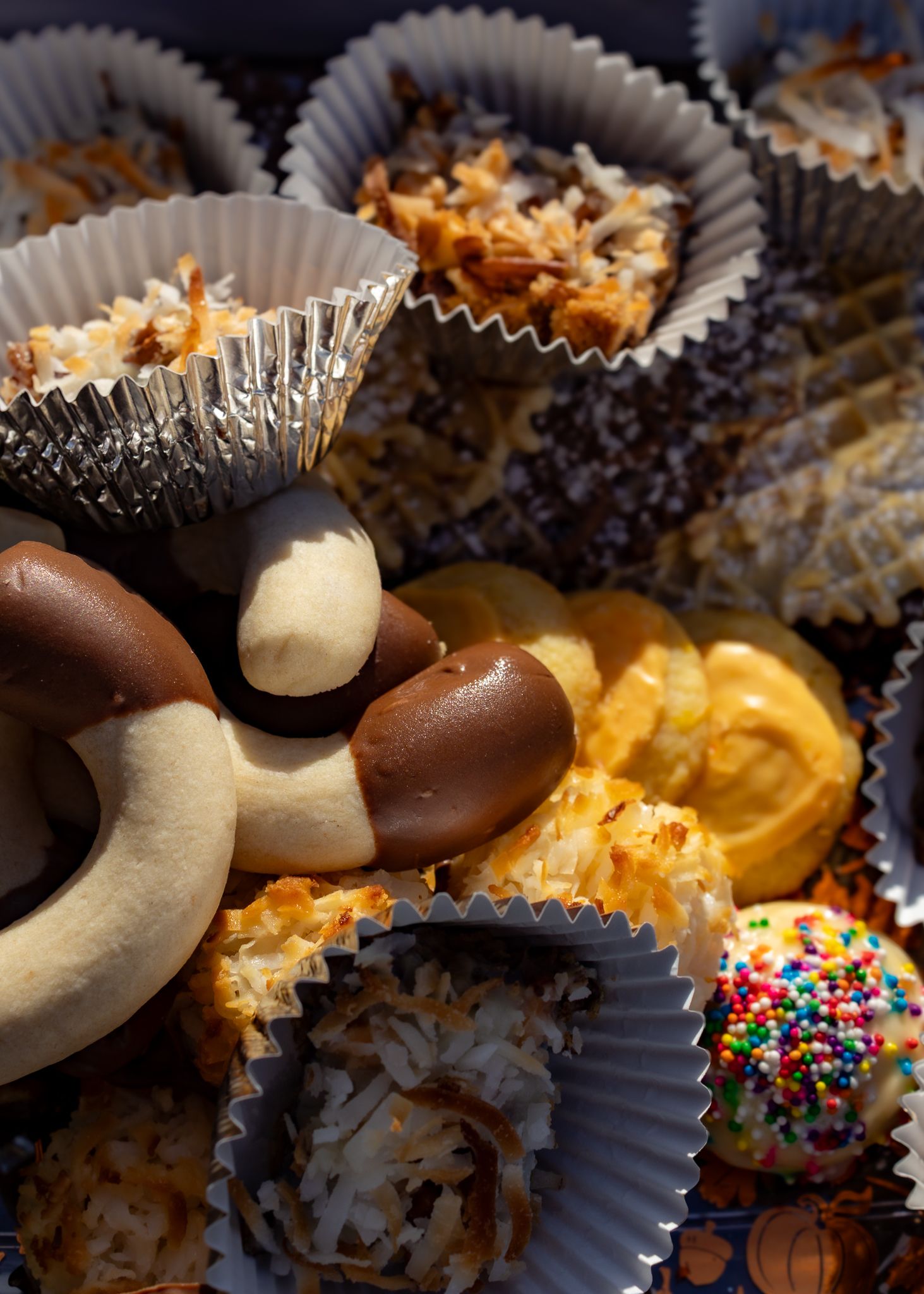 Assorted holiday cookies and sweets in paper cups, including coconut macaroons, chocolate pretzels, and sprinkle treats.