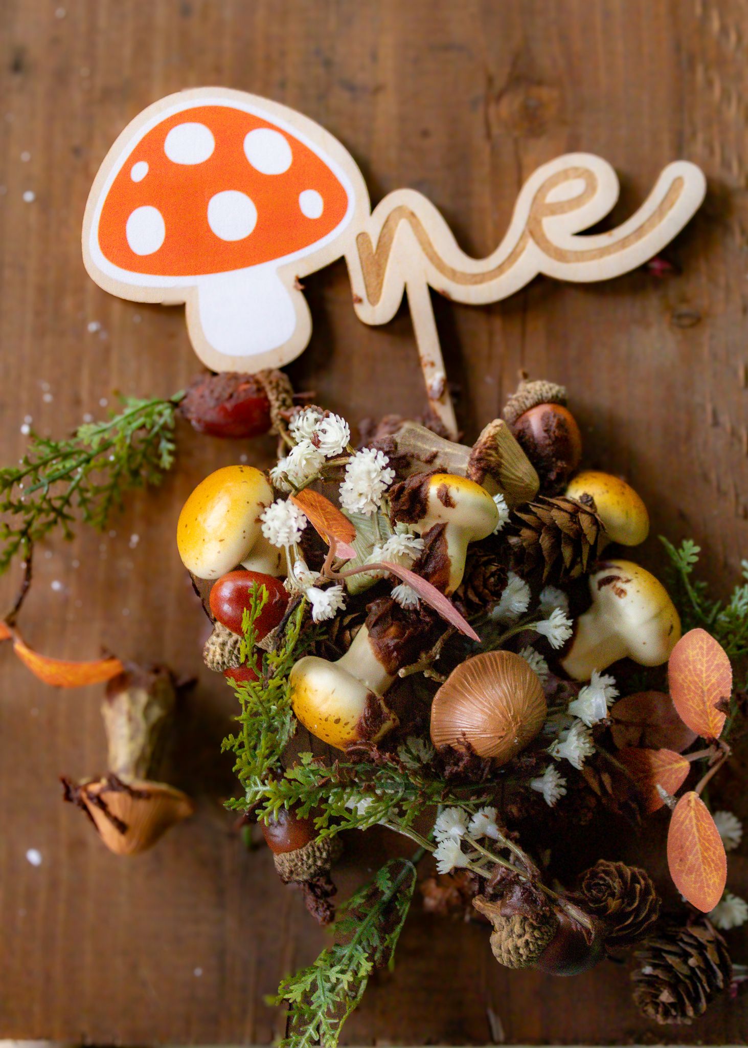 Woodland first birthday cake topper with mushroom and acorns on a rustic fall nature arrangement.