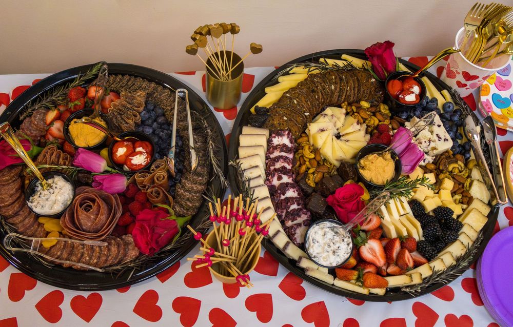 Two elegant charcuterie boards with cheese, fruits, chocolates, and dips on a Valentine's Day themed tablecloth.