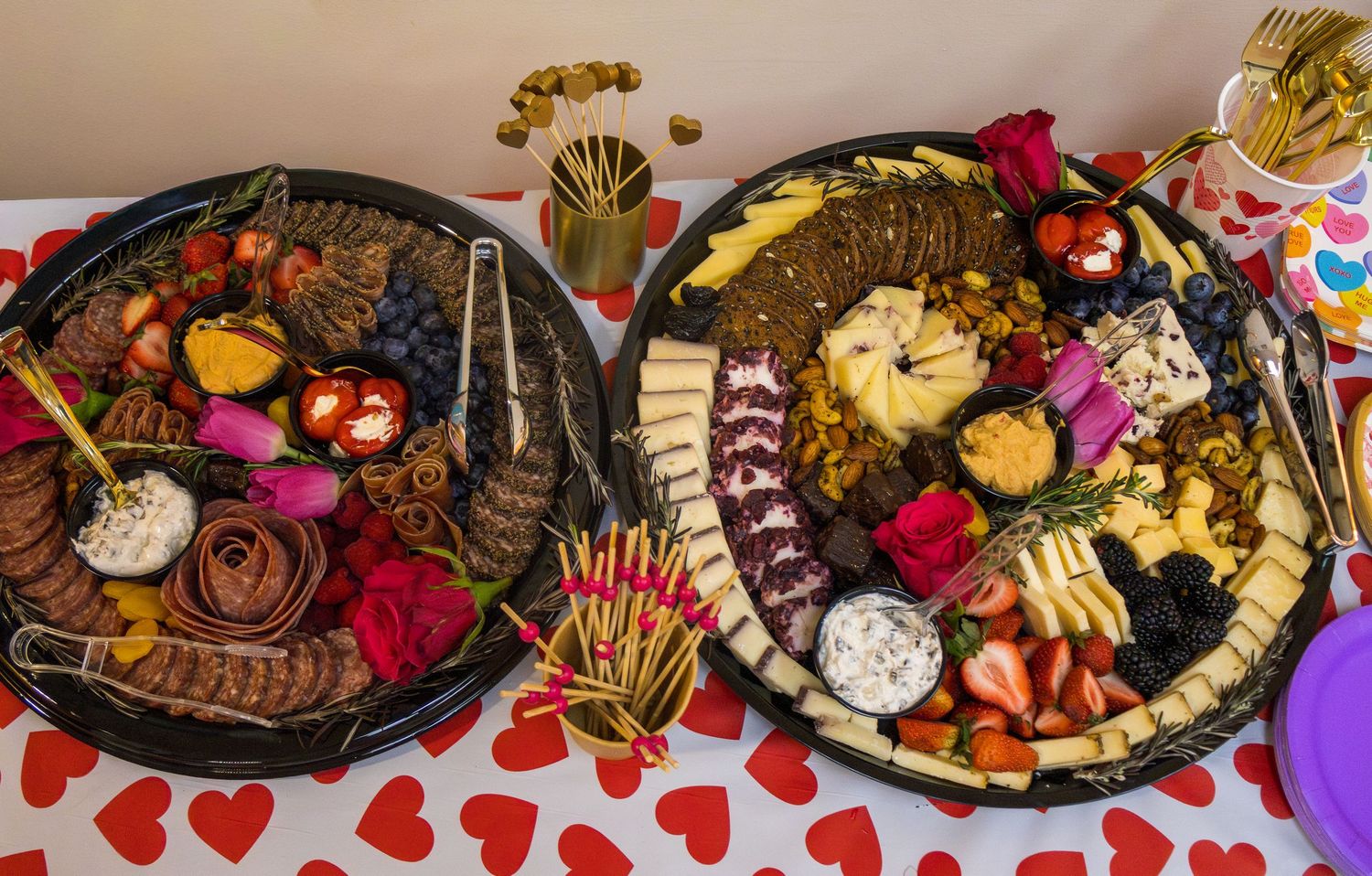 Two elegant charcuterie boards with cheese, fruits, chocolates, and dips on a Valentine's Day themed tablecloth.