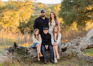 Family sitting on a fallen tree trunk during golden hour with autumn foliage in background.