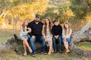 Family portrait outdoors in fall with autumn trees and golden sunlight.