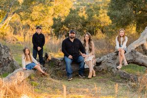 Family arranged casually on rocky ground with autumn trees in late afternoon light.
