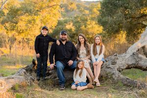 Family portrait on natural rock formation with golden fall foliage in background.