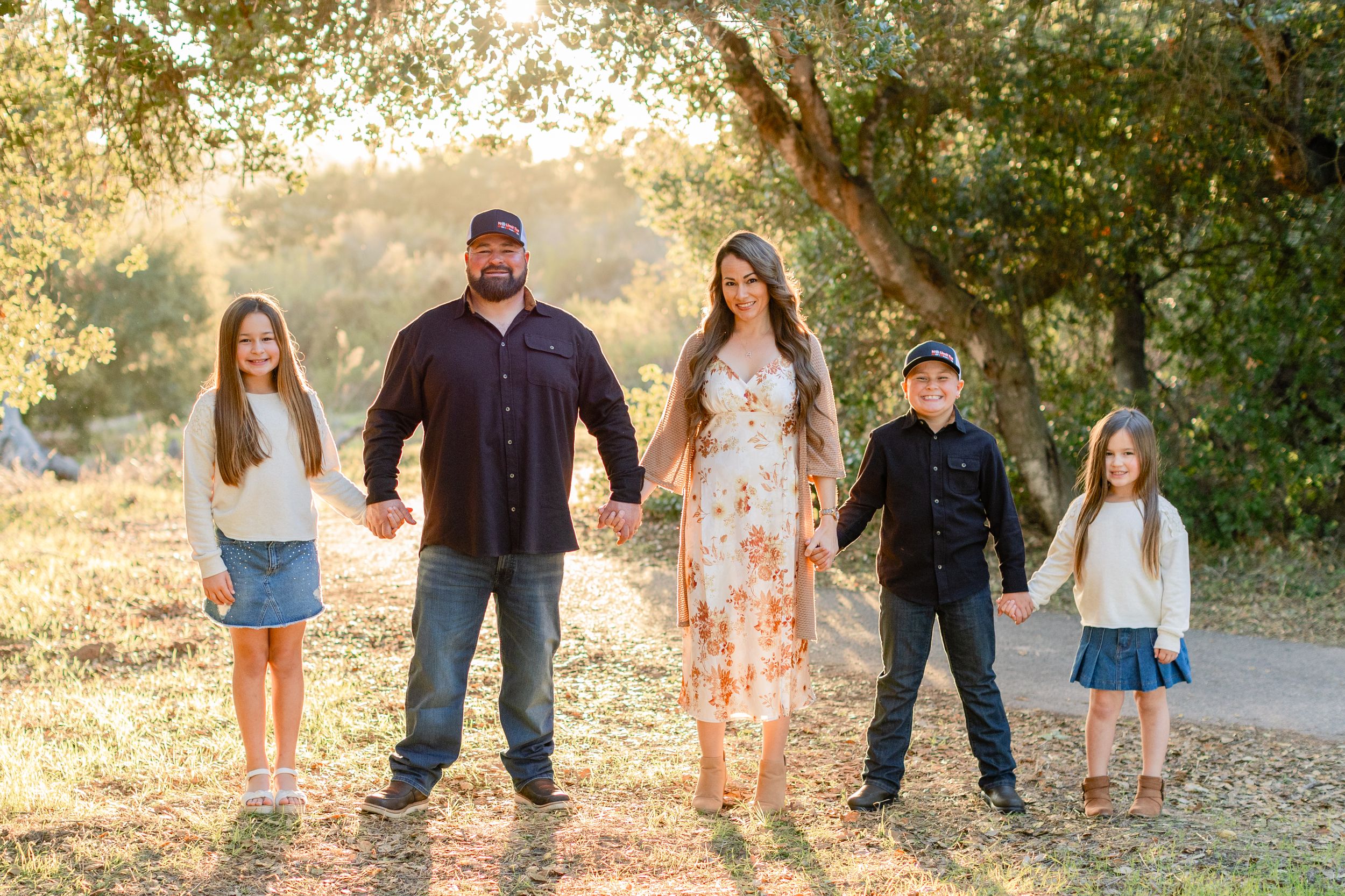 Family standing together on dirt path with sunlit trees in background.
