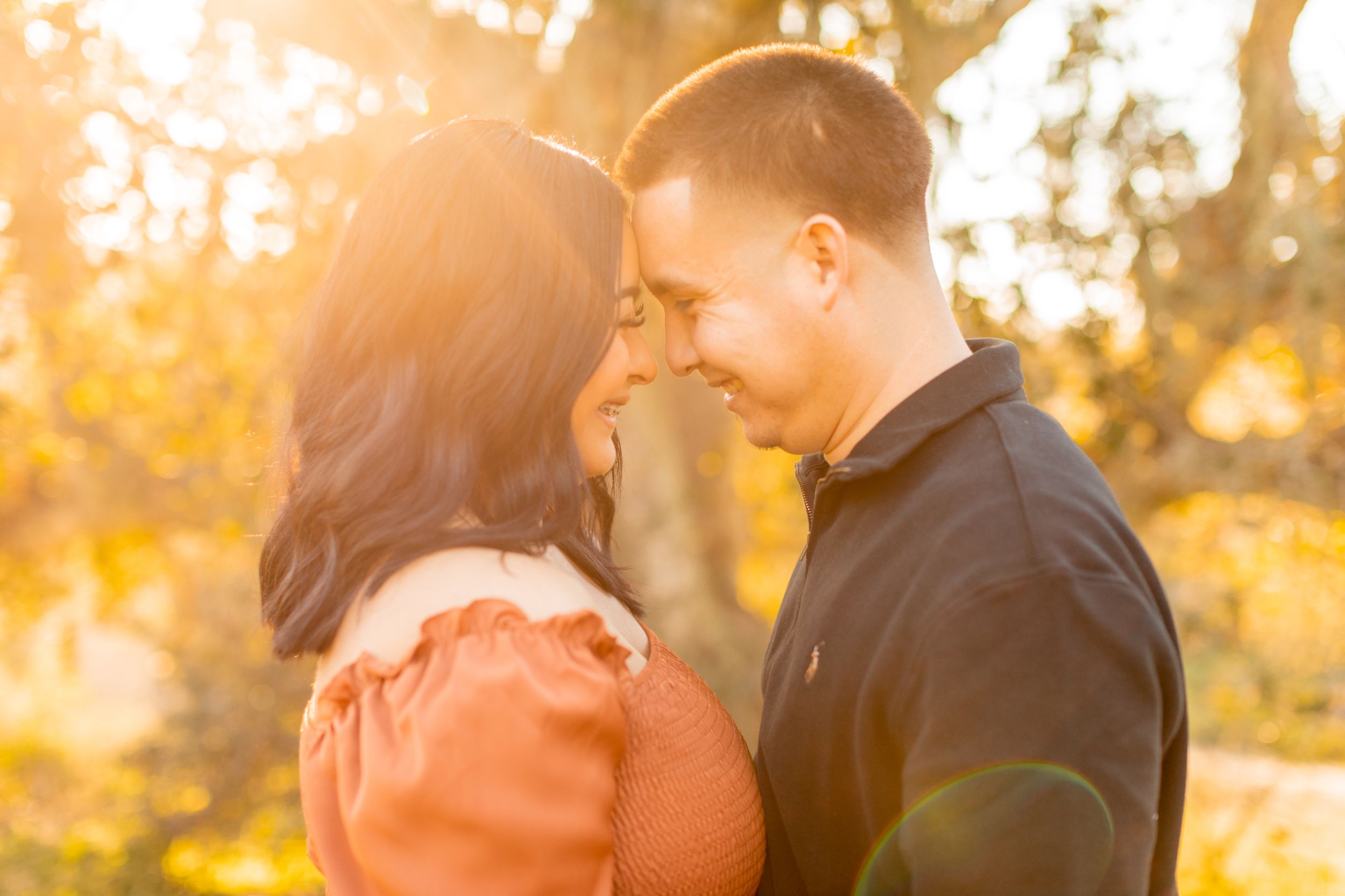 Romantic couple shares tender moment in golden autumn sunlight among trees.