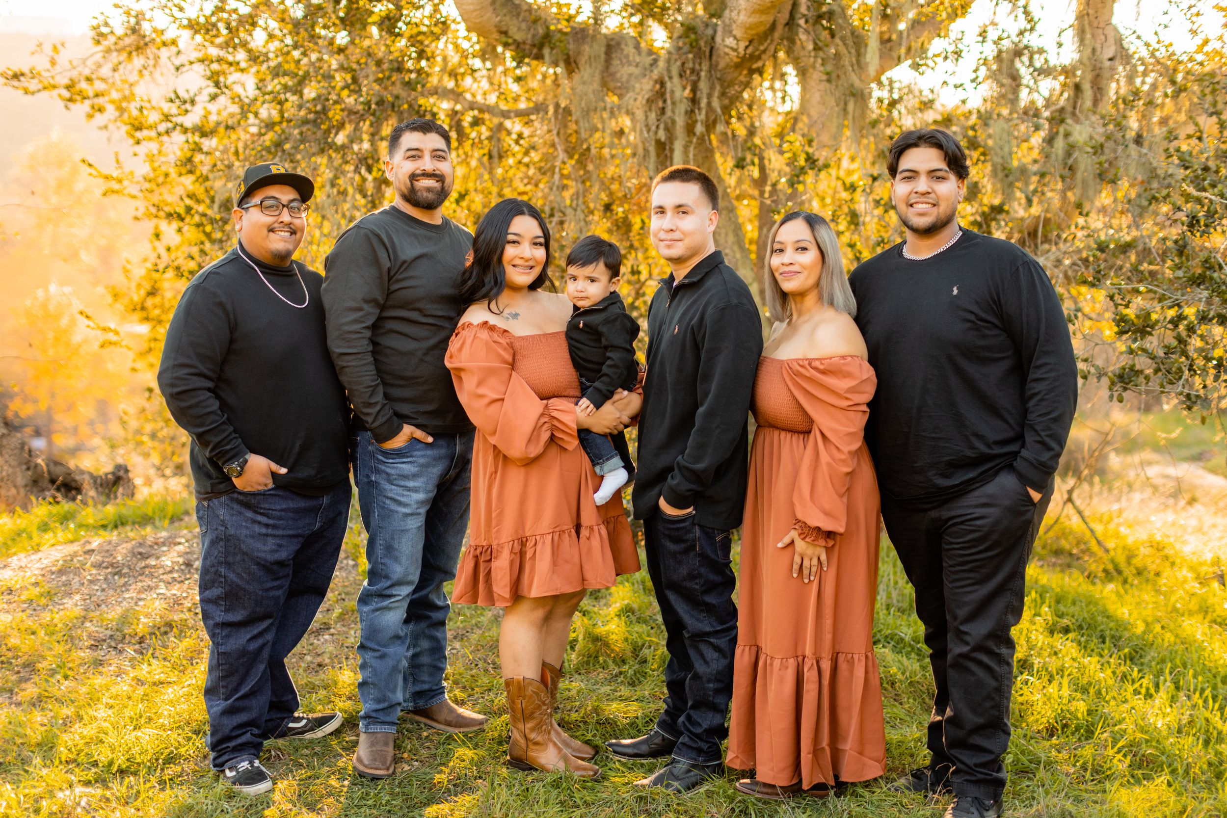 Family group in coordinated outfits poses together against golden autumn backdrop.