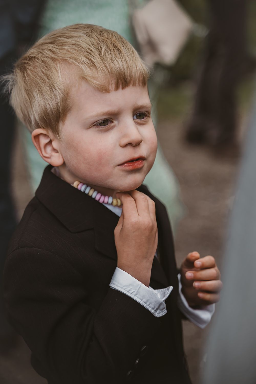 En liten pojke i svart kavaj på bröllop, han har ett godishalsband runt halsen. Bröllopsfotograf Josefin Landhagen i Östergötland, Vadstena.